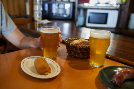 Foto de Anonymous person drinking a beer next to a croquette at a bar - Imagen libre de derechos