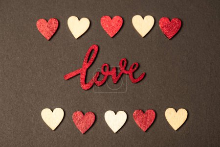 Foto de Top view composition made of bright red Love inscription placed between wooden and red shiny decorative hearts in rows on brown background - Imagen libre de derechos