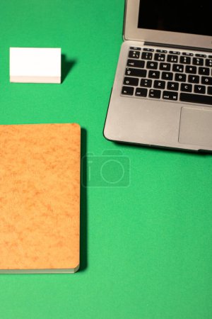 Foto de Top view of modern laptop with black screen placed on green surface close to a notebook - Imagen libre de derechos