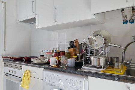 Foto de Kitchen of a house with a dirty countertop full of empty dishes and kitchen utensils for scrubbing and storage jars - Imagen libre de derechos