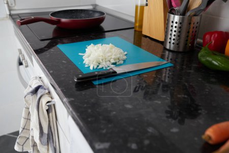 Foto de Onion sliced on a blue cutting board on a black countertop in a lighted kitchen - Imagen libre de derechos