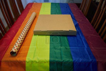 Foto de Cardboard box with hearts wrapping paper on a table with a tablecloth with the lgtbi flag - Imagen libre de derechos