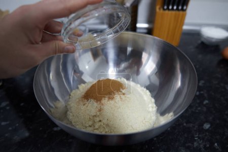 Foto de Persona anónima poniendo canela molida en un tazón con azúcar y almendras molidas - Imagen libre de derechos