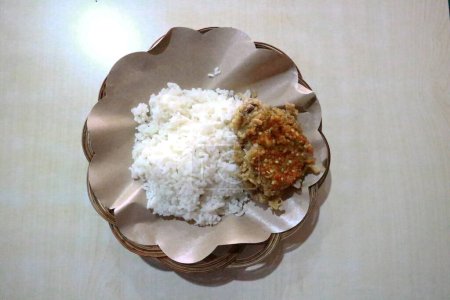 Foto de Ayam Geprek. Un plato popular indonesio, puré de pollo frito con salsa de chile de hoja de lima más arroz en un plato de ratán cubierto con papel de arroz. - Imagen libre de derechos