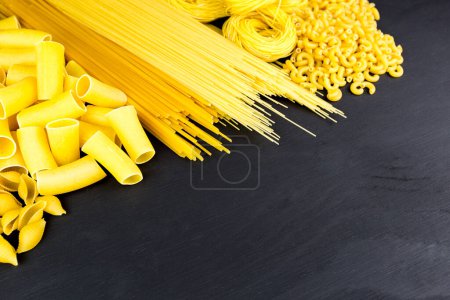 Dry pasta on black wooden background with space for text
