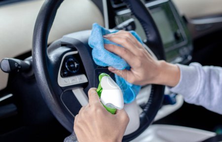 Téléchargez les photos : Car wash and interior chemical cleaning concept.hand use microfiber cloth and spray to clean lateral door from inside,retractable rear view mirror,steering wheel.modern hybrid vehicle clean inside - en image libre de droit