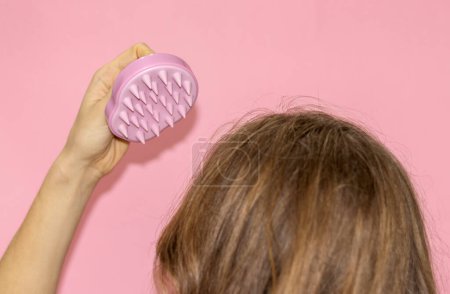 Téléchargez les photos : Blonde hair girl woman holding ponytail up or silicone soft shampoo brush with bristles isolated on pink.hair growth stimulating scalp massage healthy long curly hair.young woman back view hands up - en image libre de droit