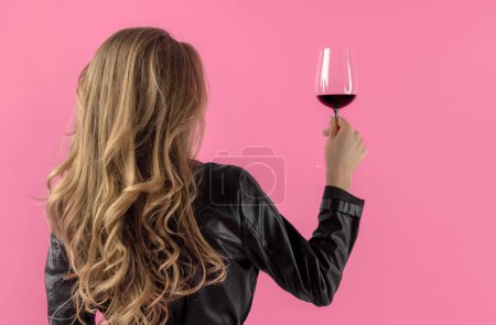 Attractive woman taking glass with wine from floor pink background.girl in black leather and sandals jacket with tulips bouquet sitting on chair.female taking photos picture of composition