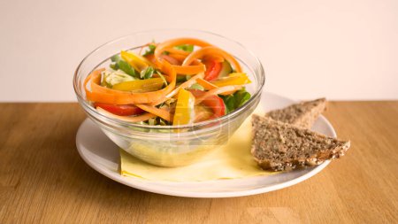Foto de Ensalada deliciosa con zanahorias y verduras servidas en un tazón con un pedazo de pan tostado al lado. - Imagen libre de derechos