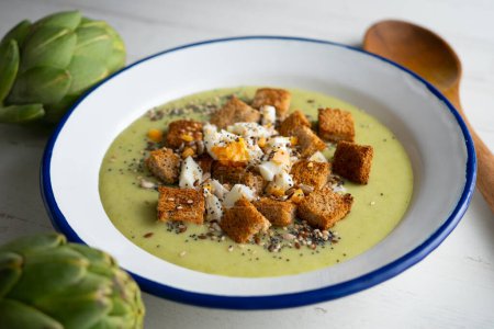 Foto de Crema de alcachofa casera hecha con caldo de verduras y patatas y decorada con croutons y huevo. - Imagen libre de derechos