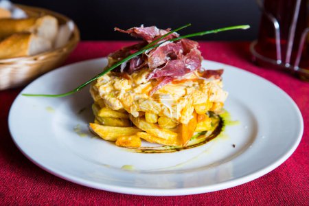 Photo for Fried eggs with chips and serrano ham. Traditional Spanish tapa nicknamed Huevos Rotos. - Royalty Free Image