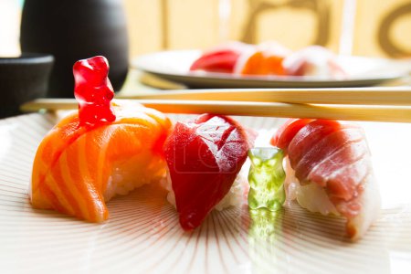 Téléchargez les photos : Ours en gomme jouant sur une table à manger avec trois sushis nigiris. - en image libre de droit