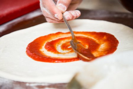 Photo for Preparing a pizza by kneading the dough and cooking with Italian homemade tomato sauce. - Royalty Free Image