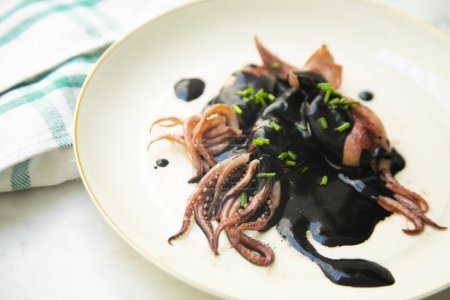 Foto de Tapa tradicional española con calamares también llamados chipirones cocinados en tinta de calamares. - Imagen libre de derechos