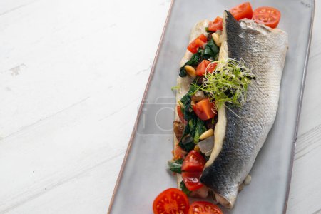 Photo for Baked sea bass stuffed with spinach, tomatoes and pine nuts. - Royalty Free Image