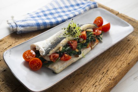 Photo for Baked sea bass stuffed with spinach, tomatoes and pine nuts. - Royalty Free Image