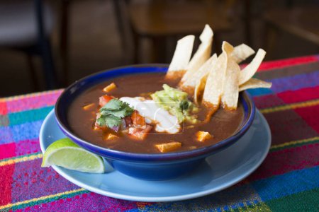 Foto de La sopa de tortilla, también llamada sopa azteca, es una sopa tradicional mexicana. La sopa se hace con caldo de tomates molidos, ajo y cebolla, sazonada con epazote, y se sirve con tiras fritas de maíz. - Imagen libre de derechos
