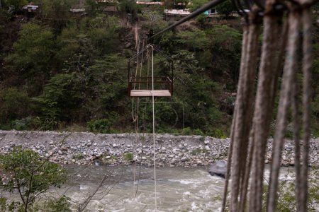 Téléchargez les photos : Oroya pour transporter du matériel ou des personnes dans une rivière dans la jungle péruvienne. Panier suspendu à deux anneaux, qui longe une corde. - en image libre de droit