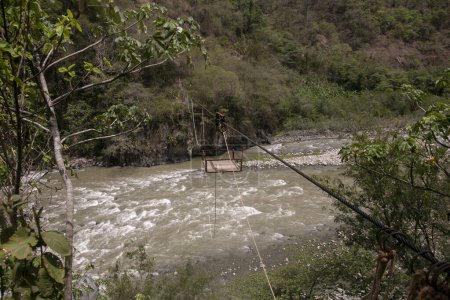 Téléchargez les photos : Oroya pour transporter du matériel ou des personnes dans une rivière dans la jungle péruvienne. Panier suspendu à deux anneaux, qui longe une corde. - en image libre de droit