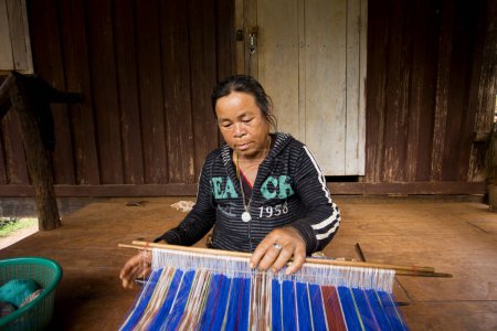 Téléchargez les photos : Chiang Rai, Thaïlande ; 1er janvier 2023 : Une femme d'une tribu indigène des hautes montagnes du district de Chiang Rai tissant du tissu à la main d'une manière artisanale. - en image libre de droit