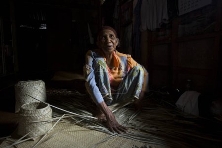 Foto de Koh Yao, Tailandia; 1 de enero de 2023: Mujer mayor haciendo una cesta con hojas de palma secas. - Imagen libre de derechos