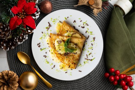 Photo for Crepe filled with pieces of banana marinated in lime juice on a table with Christmas decoration elements. - Royalty Free Image