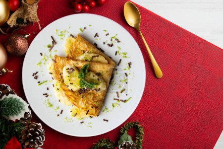 Téléchargez les photos : Crêpe remplie de morceaux de banane marinés au jus de citron vert sur une table avec des éléments de décoration de Noël. - en image libre de droit