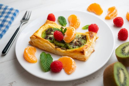 Téléchargez les photos : Tartelette feuilletée à la crème pâtissière et kiwi décoré de fruits frais. - en image libre de droit