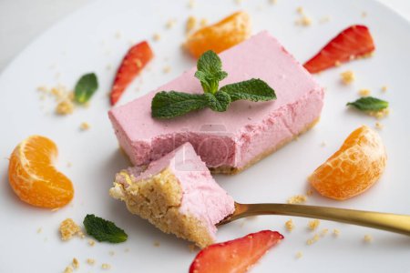 Téléchargez les photos : Portion de mousse de fraise avec une base de biscuits servie avec des fruits frais et de la mandarine. - en image libre de droit