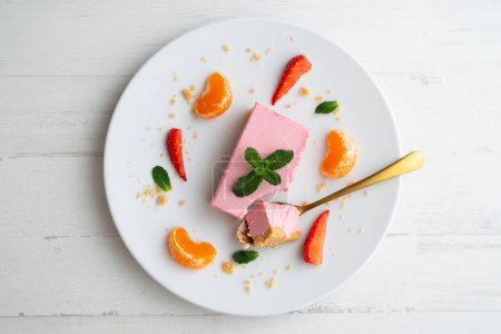 Téléchargez les photos : Portion de mousse de fraise avec une base de biscuits servie avec des fruits frais et de la mandarine. - en image libre de droit