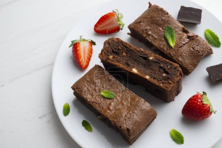 Téléchargez les photos : Brownie au chocolat coupé en portions et décoré de fraises et de menthe. - en image libre de droit