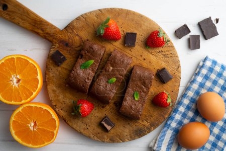 Téléchargez les photos : Brownie au chocolat coupé en portions et décoré de fraises et de menthe. - en image libre de droit