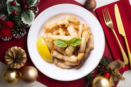 Téléchargez les photos : Tapa espagnol traditionnel. Rabas, délicieux calamar frit au citron. Nourriture de Noël servie sur une table décorée de motifs de Noël. - en image libre de droit