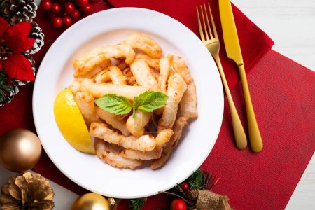 Photo for Traditional spanish tapa. Rabas, tasty fried squid with lemon. Christmas food served on a table decorated with Christmas motifs. - Royalty Free Image
