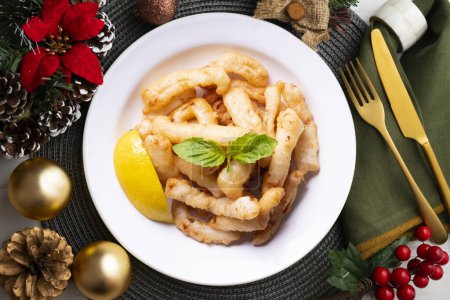 Photo for Traditional spanish tapa. Rabas, tasty fried squid with lemon. Christmas food served on a table decorated with Christmas motifs. - Royalty Free Image
