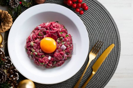 Photo for Traditional steak tartare with beef and egg yolk. Christmas food served on a table decorated with Christmas motifs. - Royalty Free Image