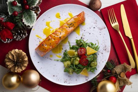 Photo for Grilled salmon with orange sauce and a salad. Typical Mediterranean coast dish. Christmas food served on a table decorated with Christmas motifs. - Royalty Free Image