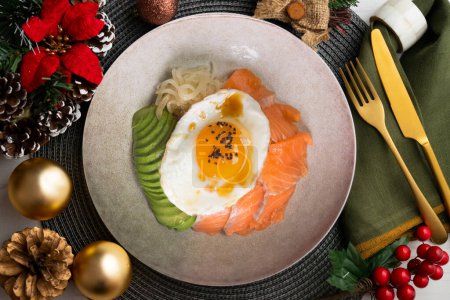 Photo for Teriyaki salmon donburi with fried egg, avocado, onion, red pepper and other vegetables. Christmas food served on a table decorated with Christmas motifs. - Royalty Free Image