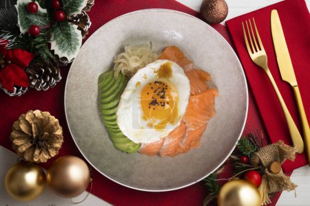 Foto de Donburi de salmón Teriyaki con huevo frito, aguacate, cebolla, pimiento rojo y otras verduras. Comida navideña servida sobre una mesa decorada con motivos navideños. - Imagen libre de derechos