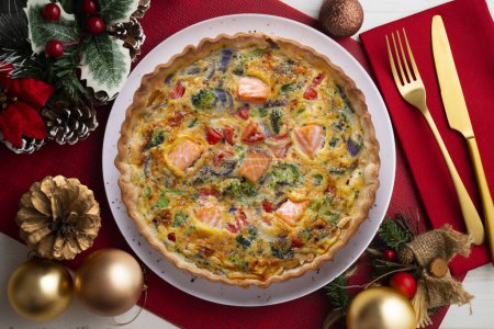 Téléchargez les photos : Quiche traditionnelle de saumon avec brocoli et légumes. Nourriture de Noël servie sur une table décorée de motifs de Noël. - en image libre de droit