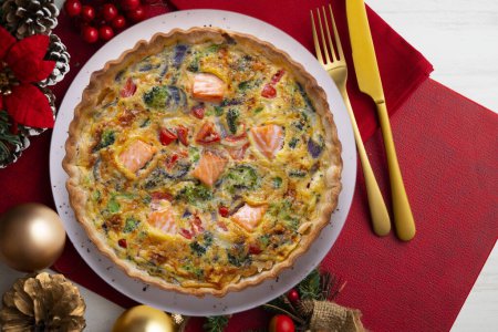 Téléchargez les photos : Quiche traditionnelle de saumon avec brocoli et légumes. Nourriture de Noël servie sur une table décorée de motifs de Noël. - en image libre de droit