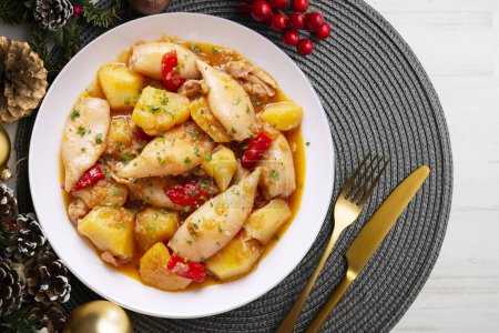 Photo for Squid stew with red peppers. Typical Spanish tapa recipe. Christmas food served on a table decorated with Christmas motifs. - Royalty Free Image