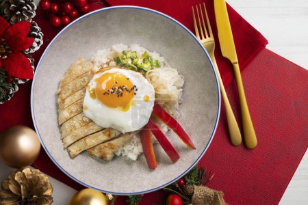 Téléchargez les photos : Donburi de poulet Teriyaki avec oeuf frit. Nourriture de Noël servie sur une table décorée de motifs de Noël. - en image libre de droit