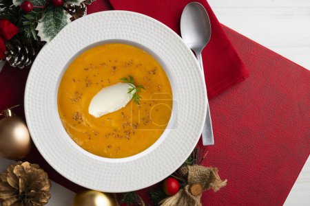 Téléchargez les photos : Crème de carotte et citrouille à la crème et aux noix. Nourriture de Noël servie sur une table décorée de motifs de Noël. - en image libre de droit