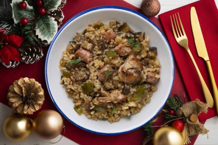 Foto de Rice paella with rabbit, sausages and green beans. Tapa traditional recipe in Valencia, Spain. Christmas food served on a table decorated with Christmas motifs. - Imagen libre de derechos