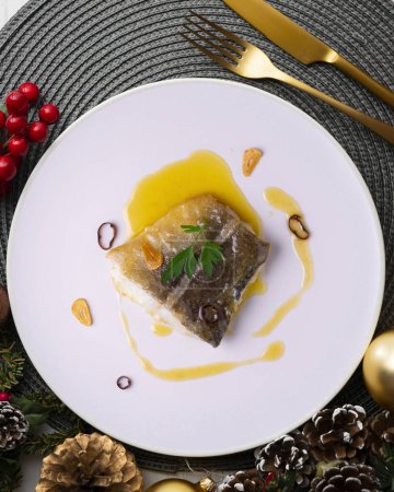 Photo for Bacalao al pil pil traditional tapa from north Spain. Codfish cooked with a delicious sauce made with oil, codfish and garlic. Christmas food served on a table decorated with Christmas motifs. - Royalty Free Image