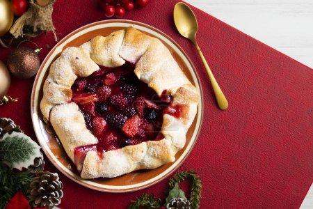 Photo for Red fruit galette with blackberries, strawberries, raspberries. Traditional French recipe. Christmas food served on a table decorated with Christmas motifs. - Royalty Free Image