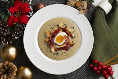 Photo for Smoked aubergine cream with crispy Iberian ham and boiled egg. Christmas food served on a table decorated with Christmas motifs. - Royalty Free Image