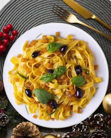 Photo for Pasta ribbons with sauted pumpkin and black olives.  Christmas food served on a table decorated with Christmas motifs. - Royalty Free Image