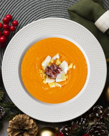 Photo for Traditional spanish salmorejo. Cold tomato soup served with egg and iberico jam. Christmas food served on a table decorated with Christmas motifs. - Royalty Free Image